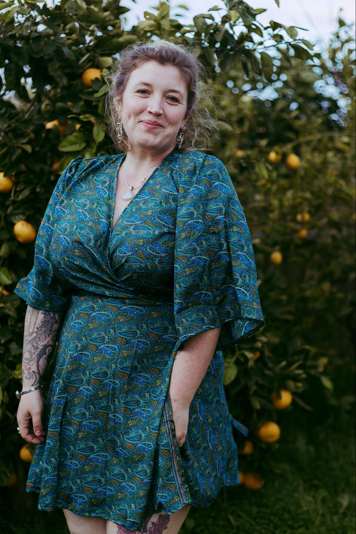Woman wearing a blue patterned dress standing in front of an orange tree