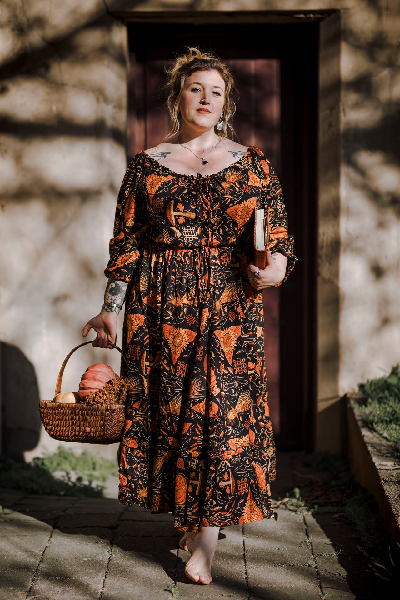 Woman in a mushroom patterned dress holding a basket of pumpkins outdoors
