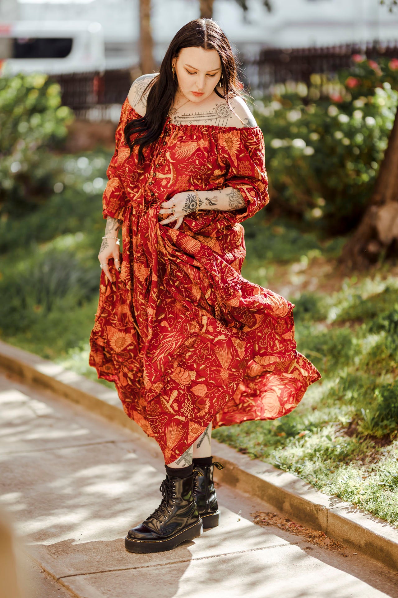 Woman in a red patterned dress walking outdoors on a wooden path.