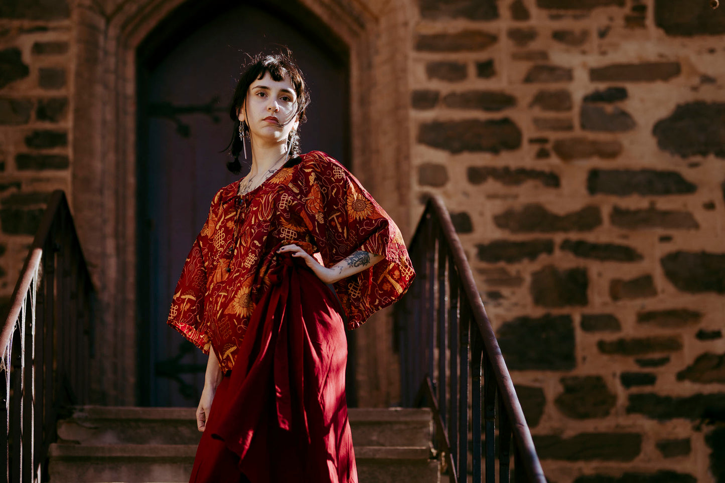 Woman in a red dress standing on stone steps with a stone wall background