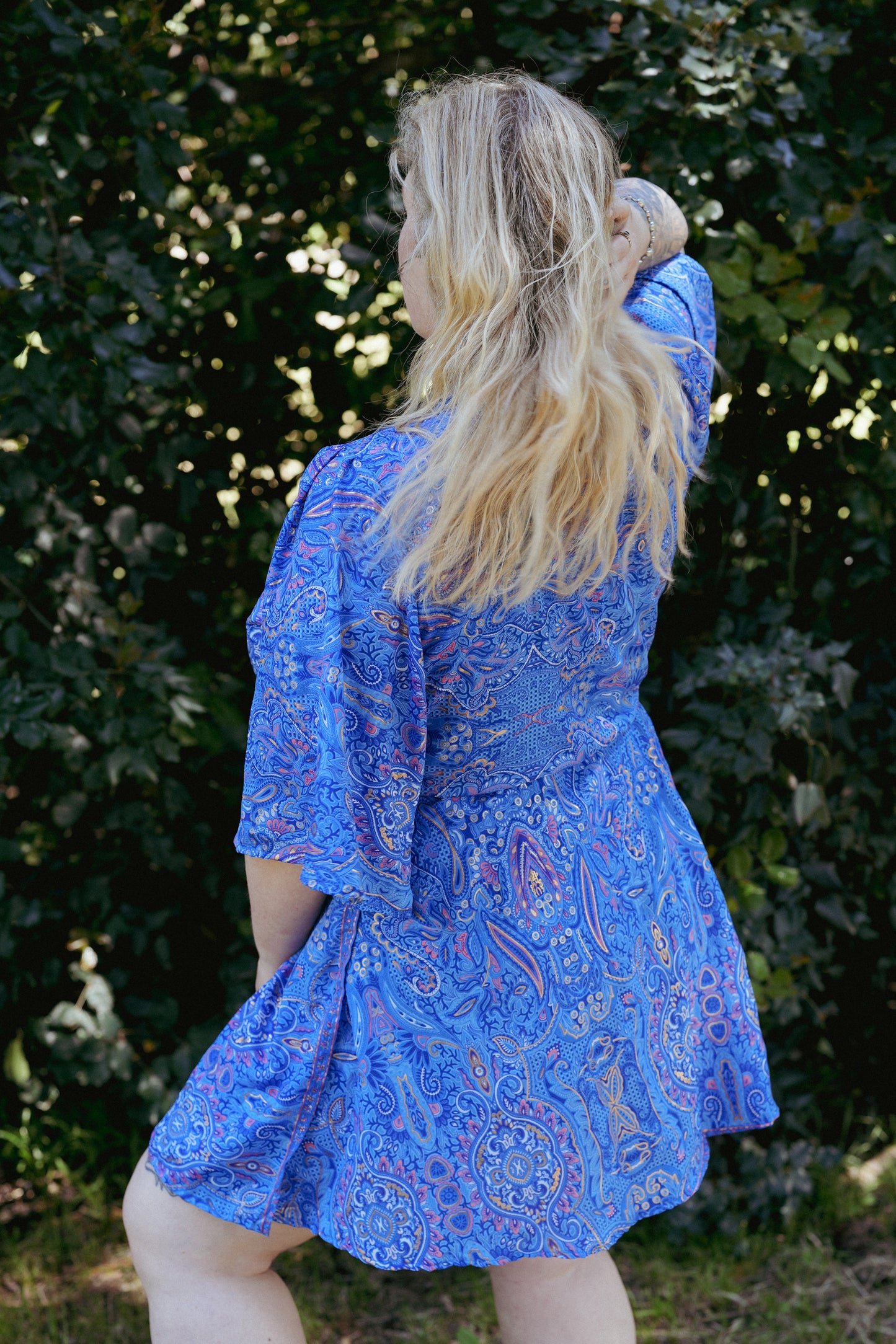 Woman wearing a blue patterned dress standing in front of green foliage