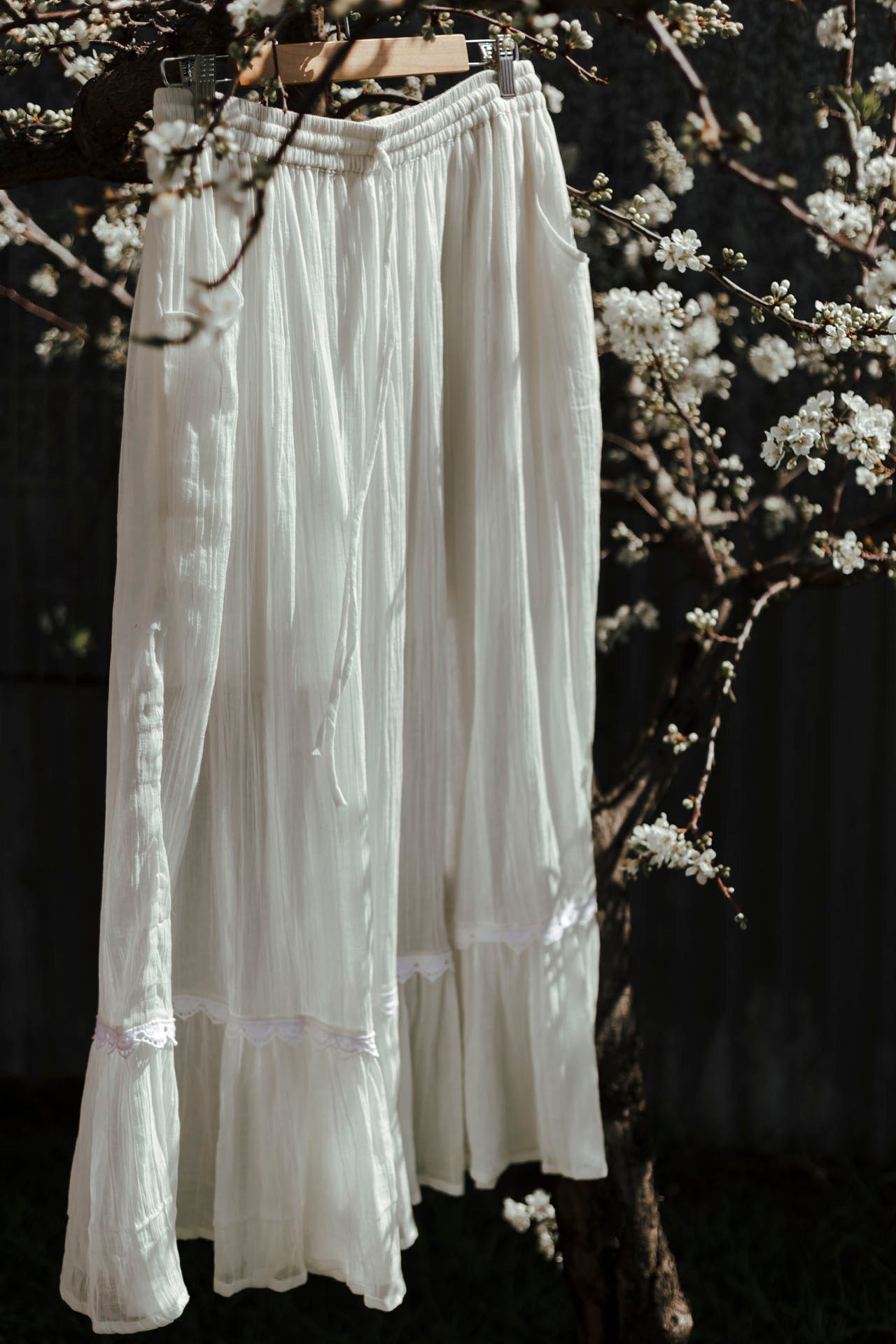 White lace skirt hanging against a dark background with floral elements