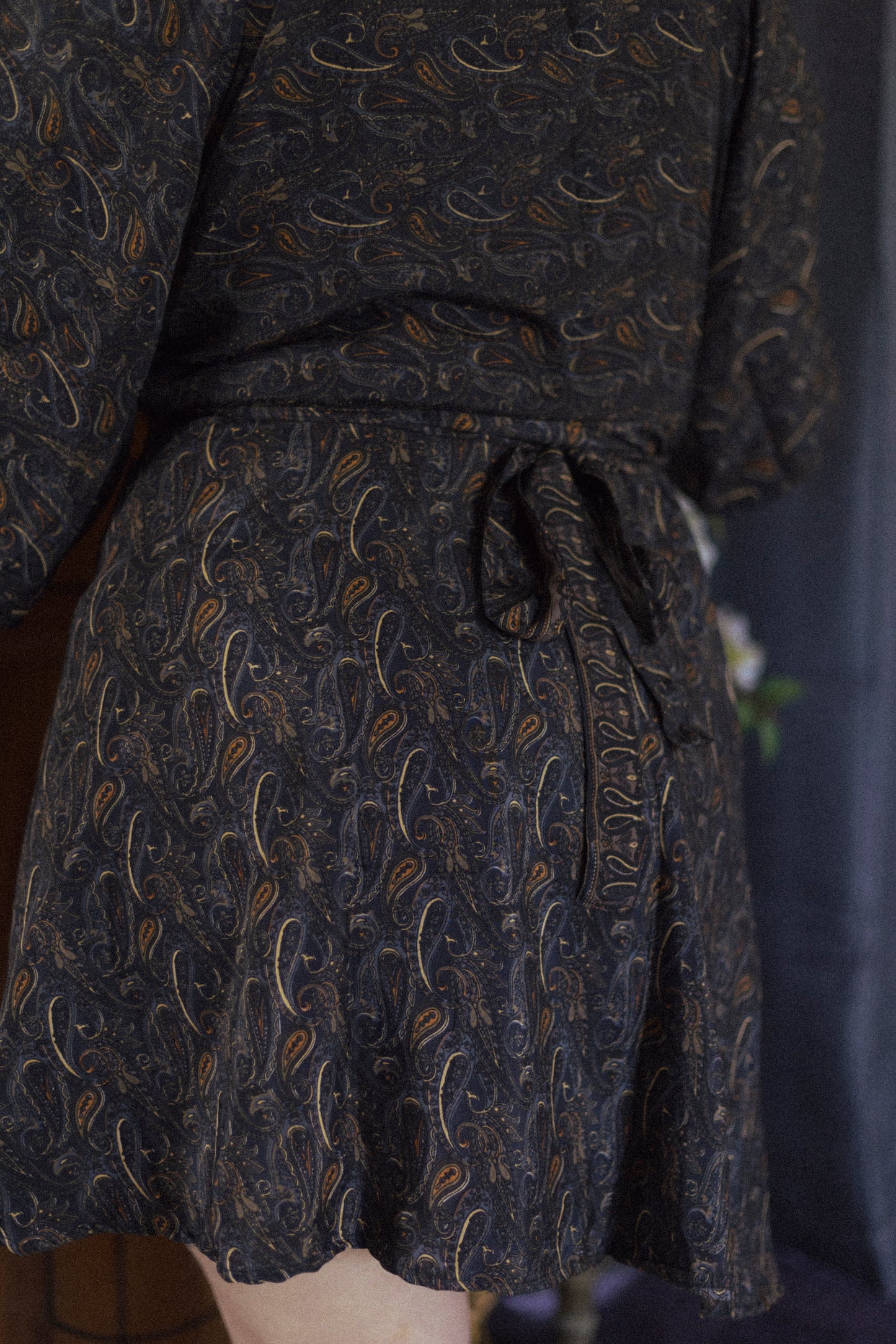 Dark patterned wrap dress tied at the waist on a plain background