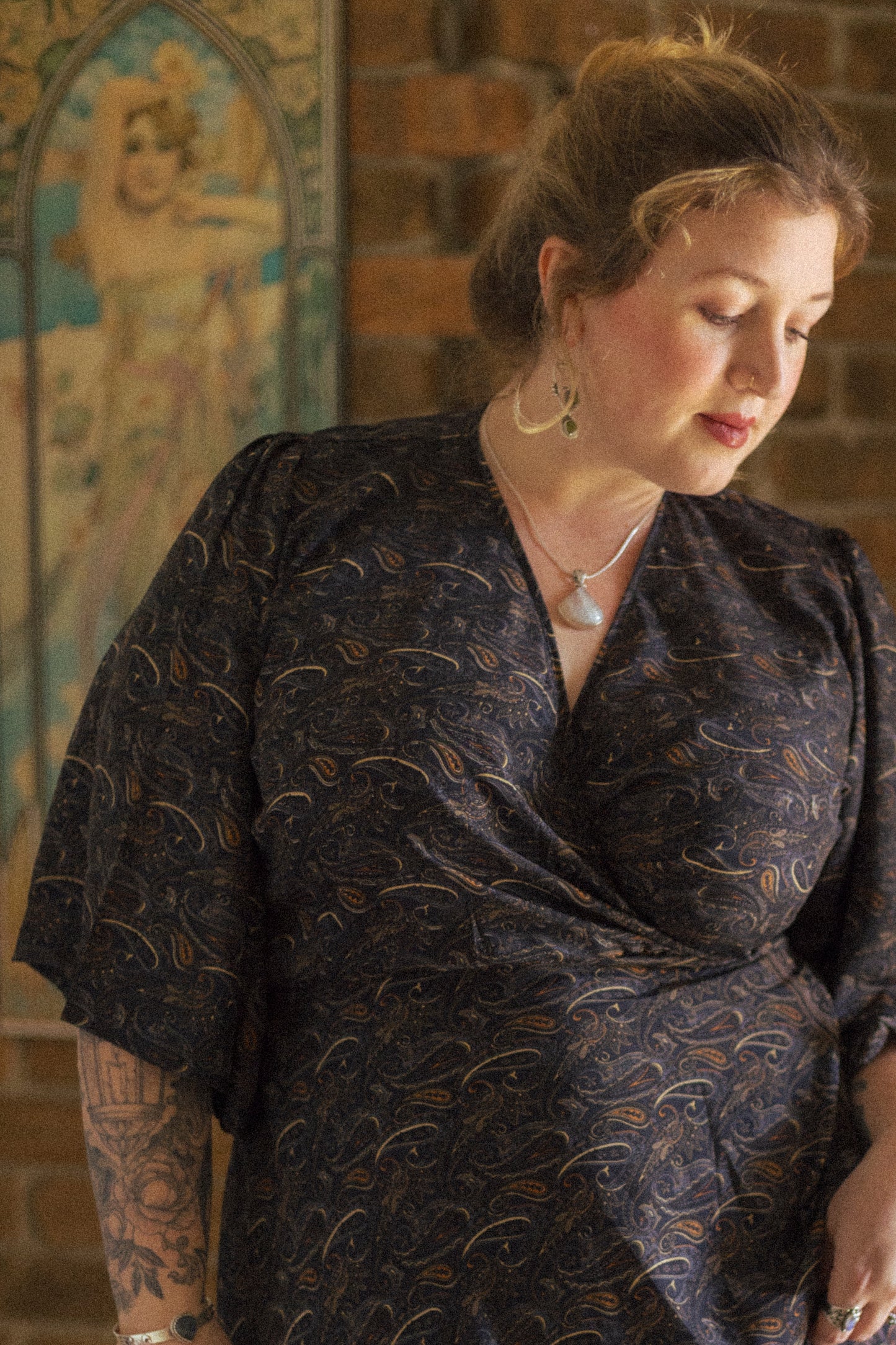 Woman wearing a dark patterned dress in front of a brick wall with decorative elements.