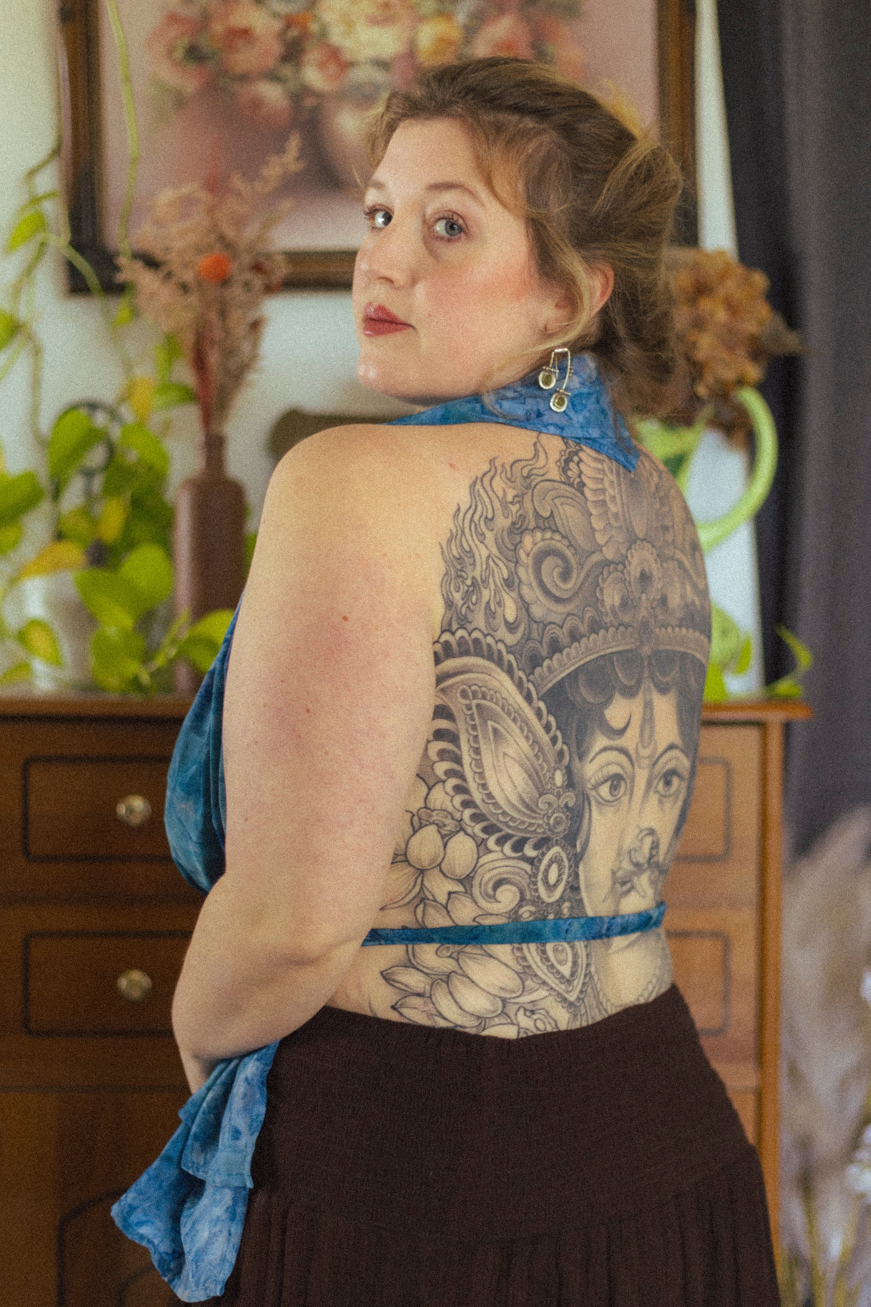 Woman with a large tattoo on her back standing indoors.