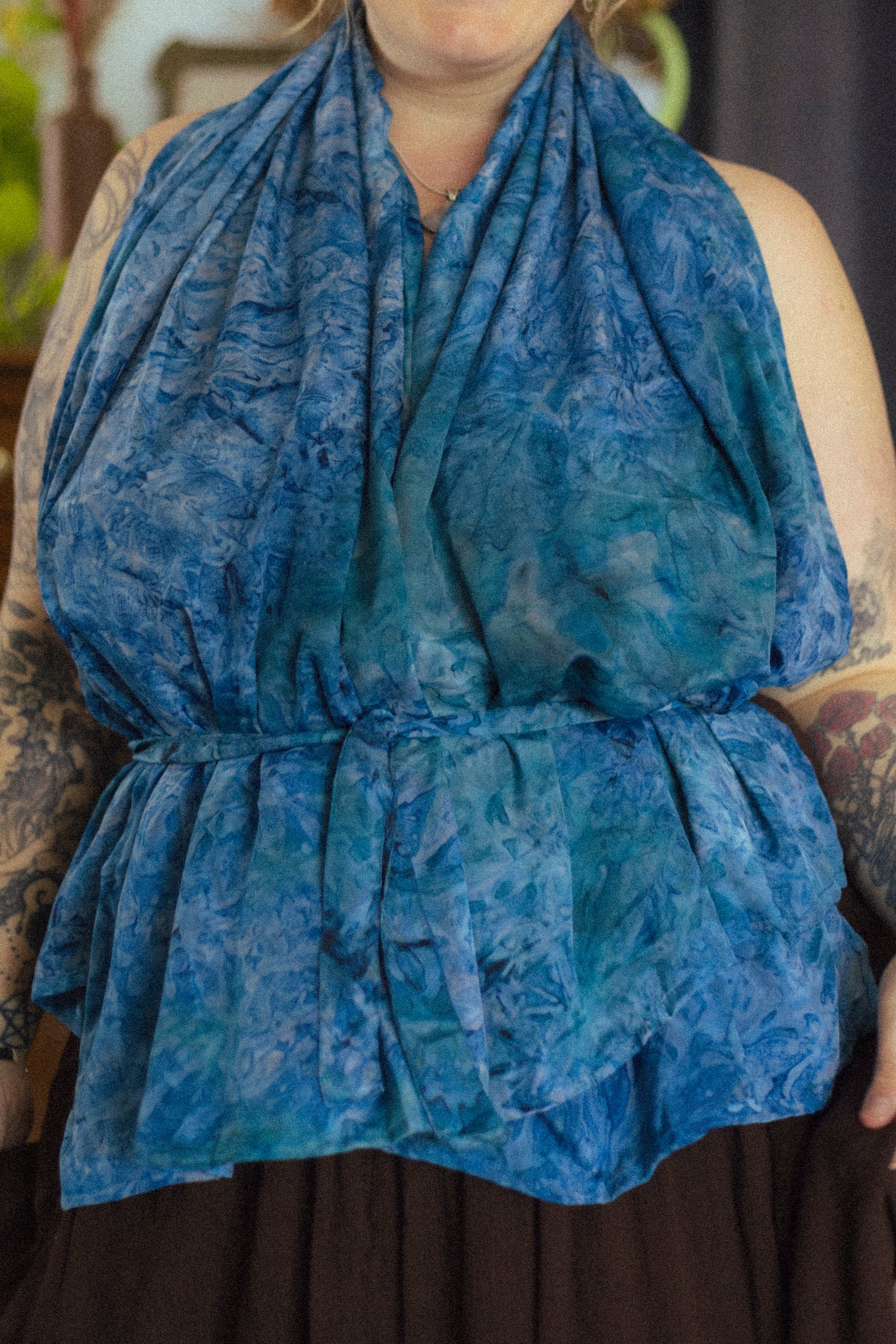 Person wearing a blue patterned scarf with tattoos on arms