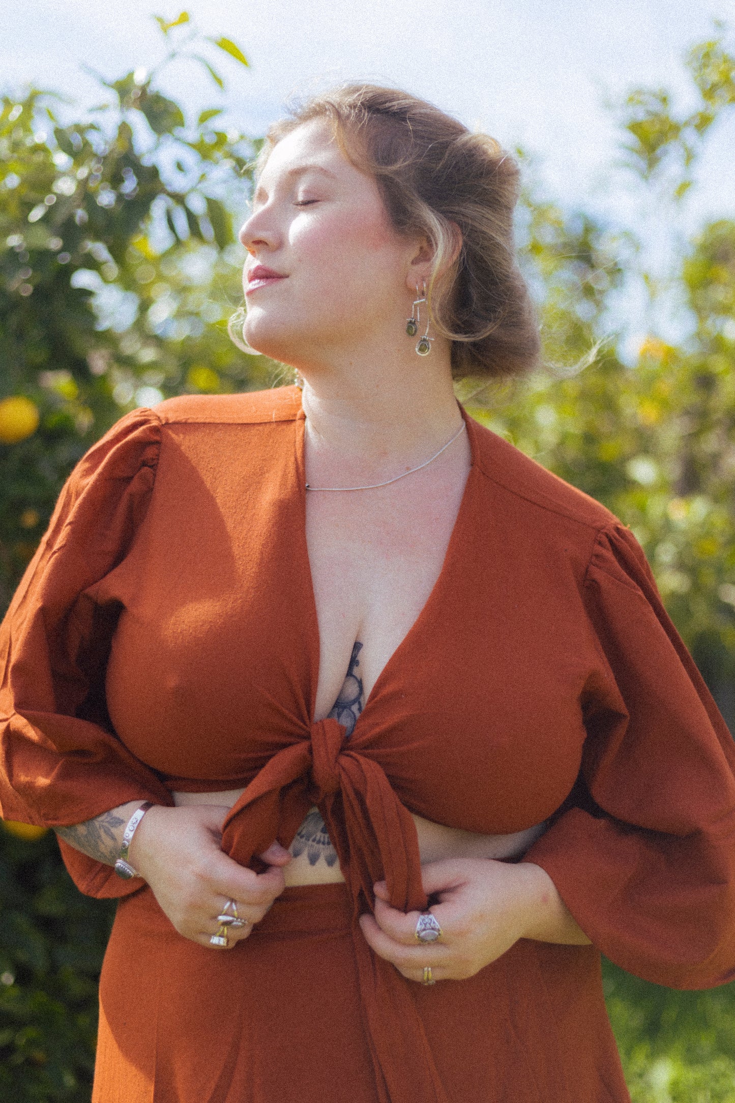 Woman wearing a rust-colored dress with puffed sleeves against a blurred green background