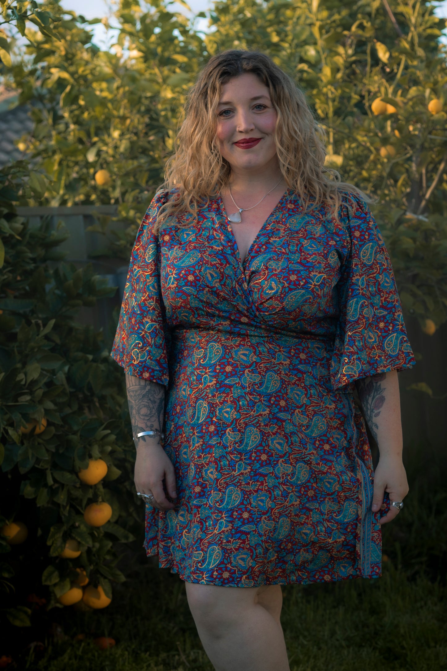 Woman wearing a floral dress standing outdoors with greenery and fruit in the background