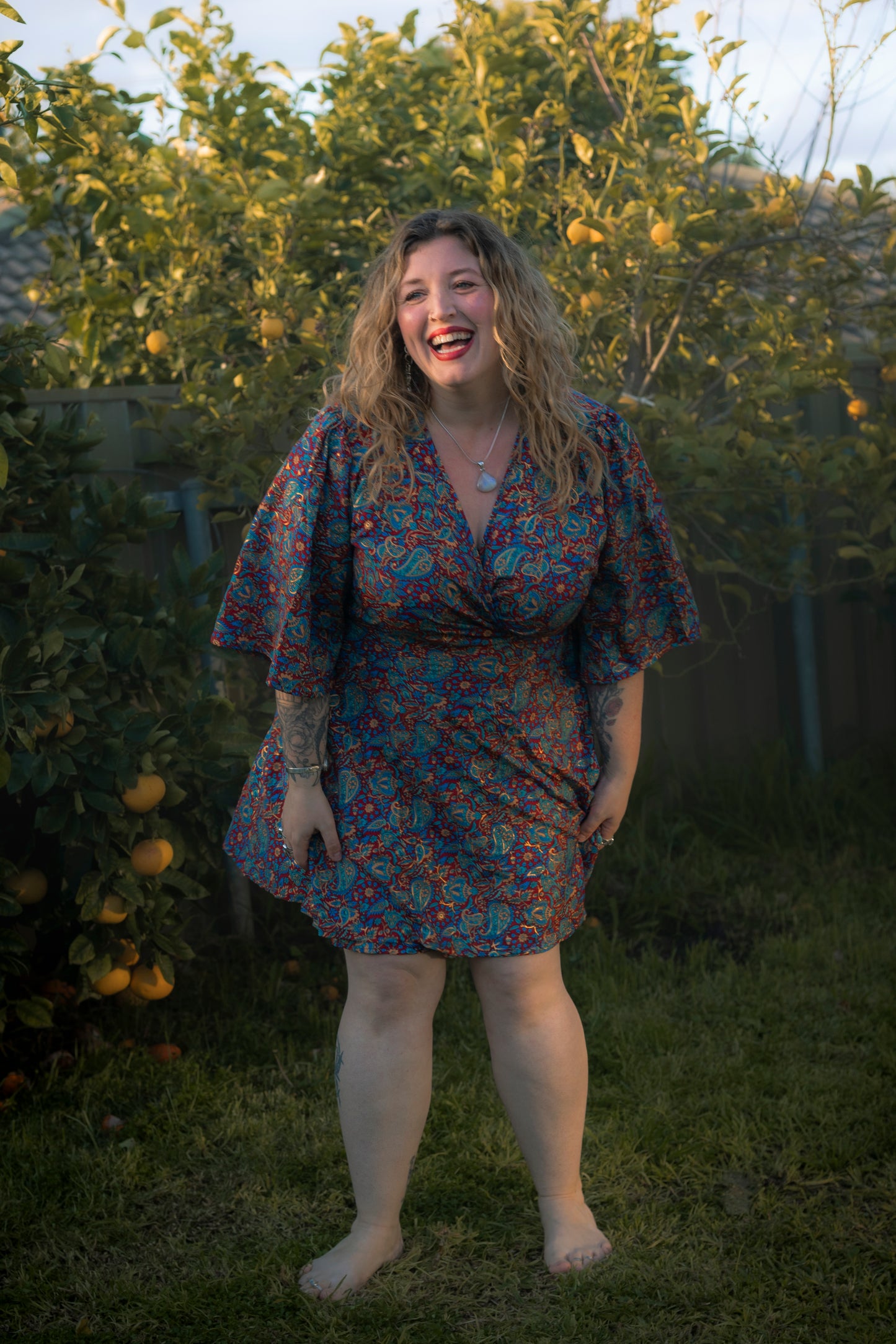 Woman laughing in a floral dress standing in a garden with trees and fruits in the background