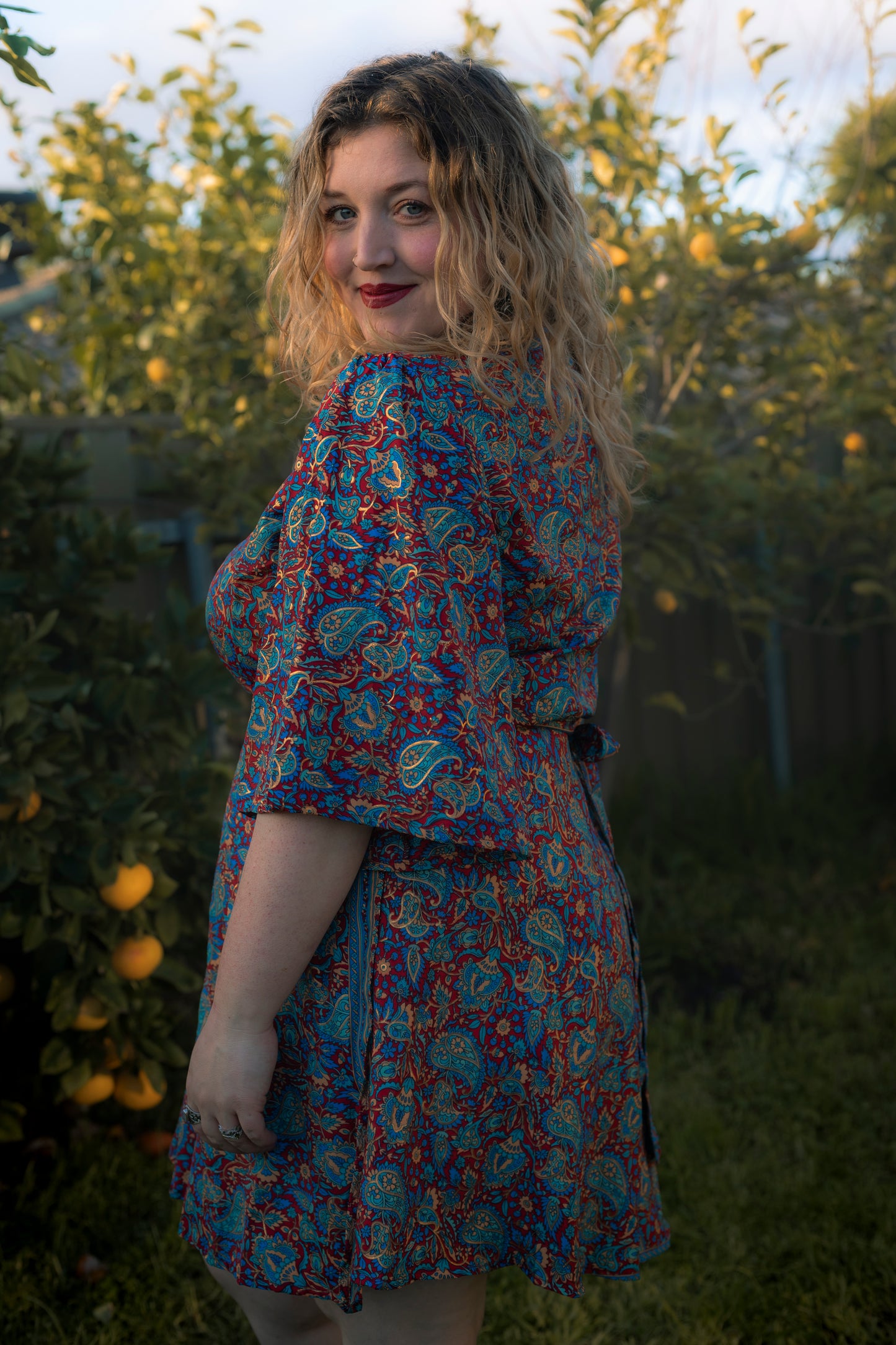 Woman wearing a colorful floral dress standing in a garden.