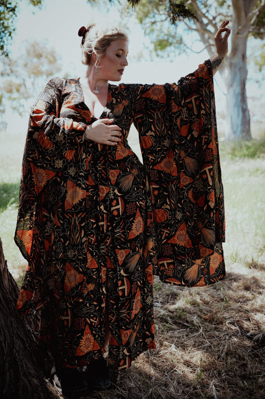 Woman in a patterned dress standing outdoors with trees in the background