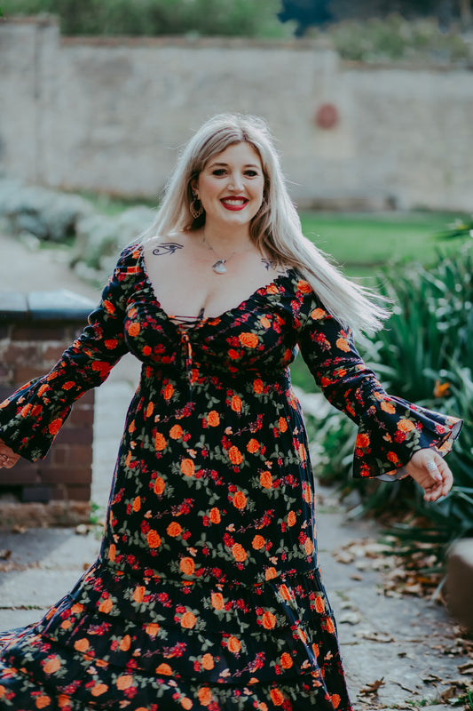 Woman in a floral dress standing outdoors with greenery in the background