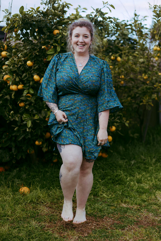 Woman in a green dress standing in an outdoor setting with trees and fruits.