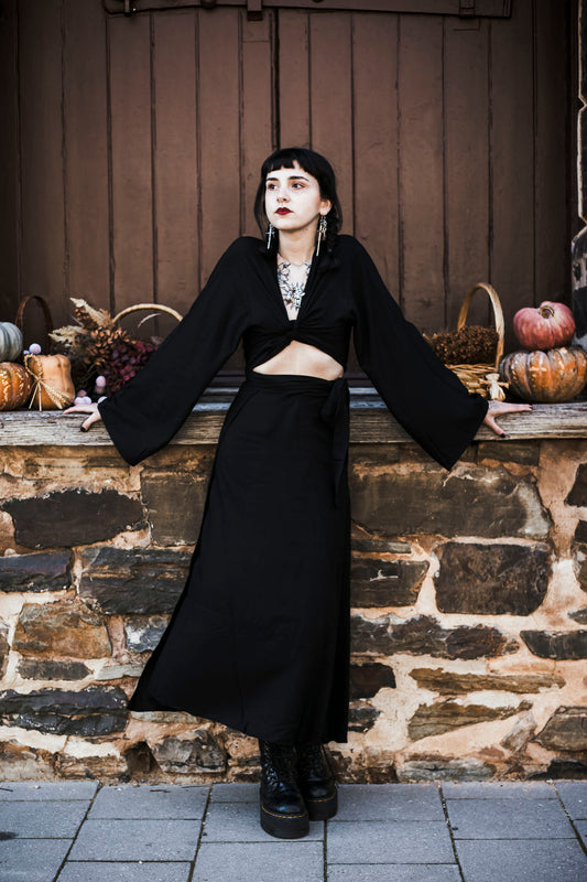 Woman in a black outfit standing against a stone wall with pumpkins.