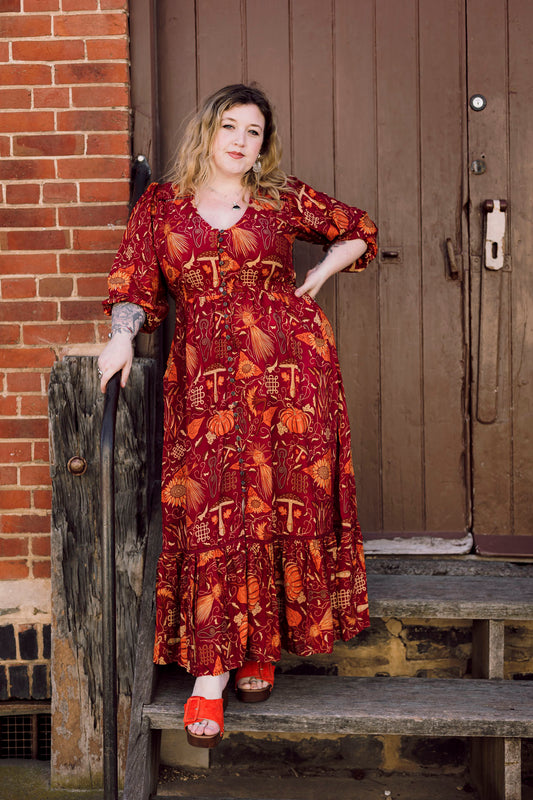 Woman in a red patterned dress standing on wooden steps against a brick wall.