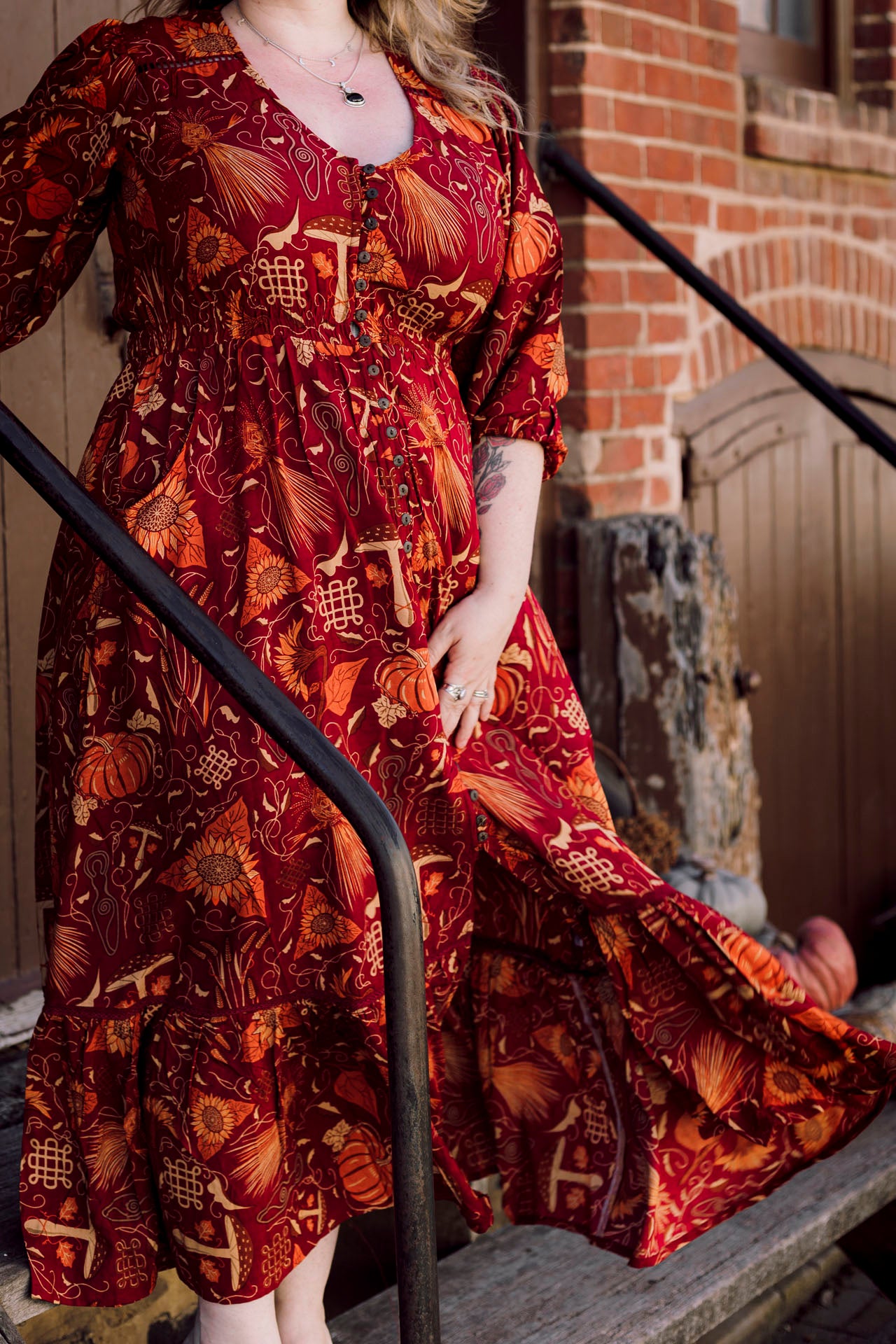 Person wearing a long, patterned dress standing on a staircase with a brick wall background.