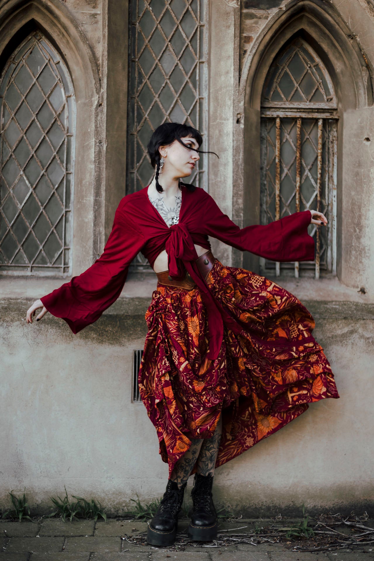 Person in a red and patterned dress with long sleeves, standing against an old building with arched windows.