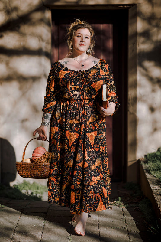 Woman in a mushroom patterned dress holding a basket of pumpkins outdoors