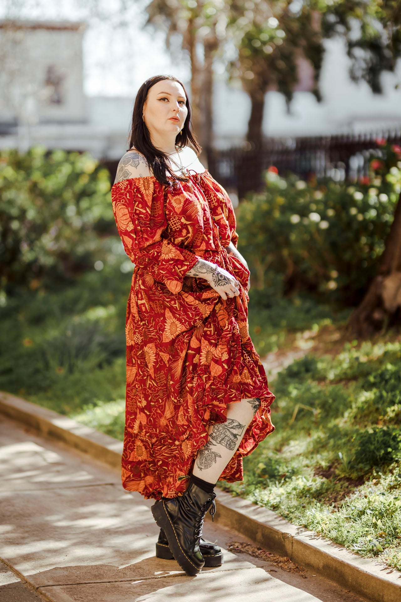 Woman in a red patterned dress standing outdoors with greenery in the background