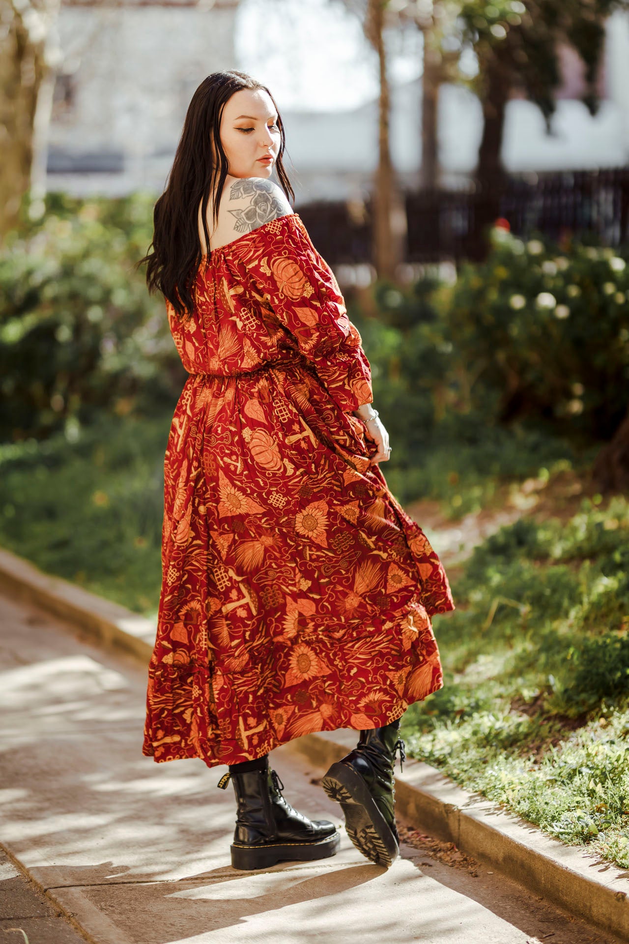 Woman in a red patterned dress walking on a sidewalk with greenery in the background