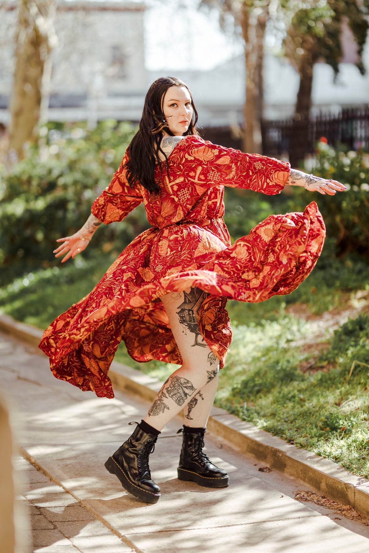 Person in a red floral dress dancing outdoors on a sunny day.
