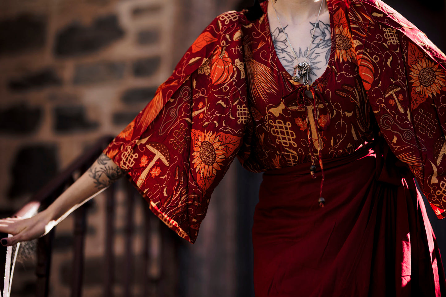 Person wearing a traditional outfit with intricate patterns against a stone wall.