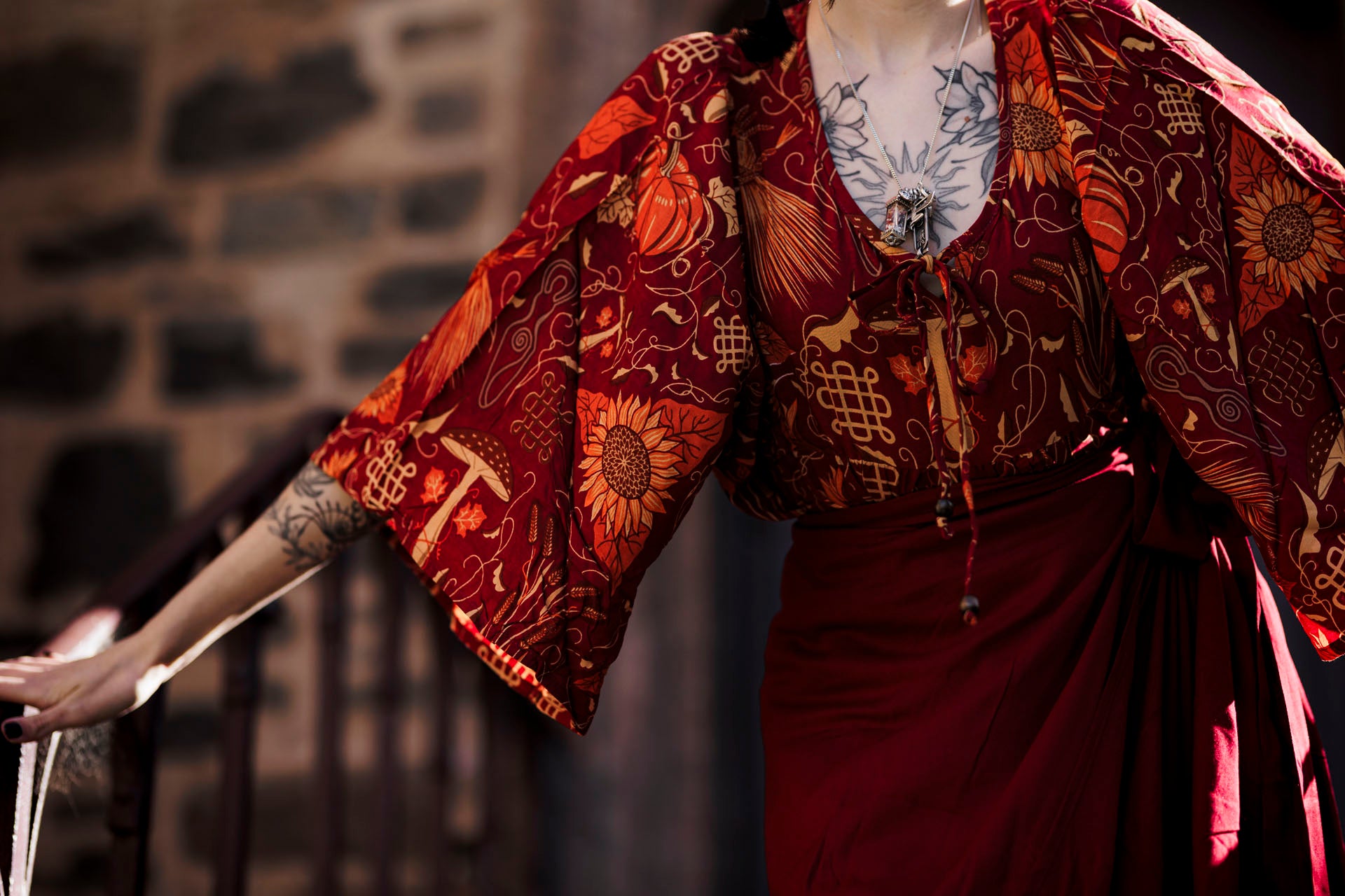 Person wearing a traditional outfit with intricate patterns against a stone wall.