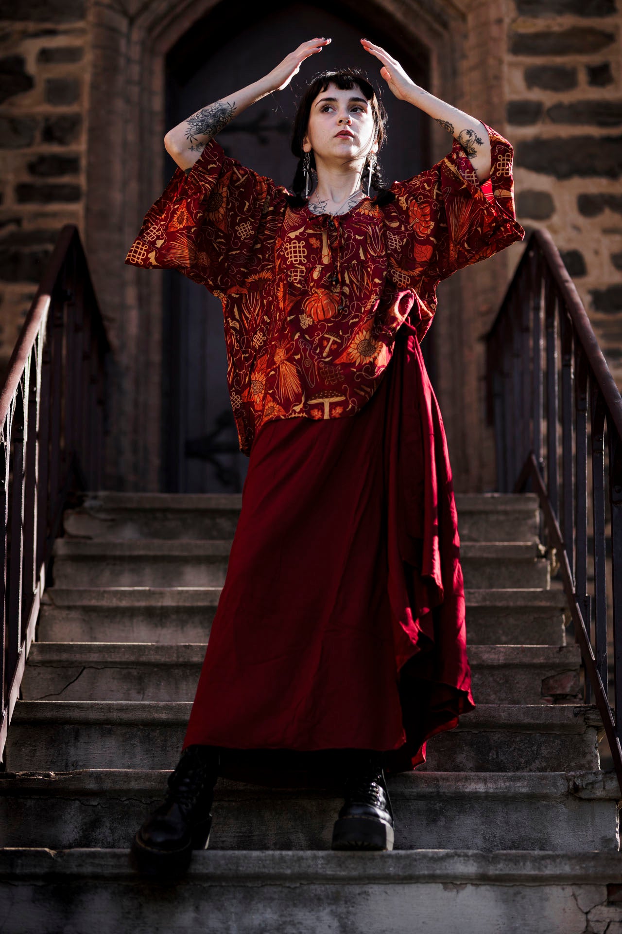 Person in a red and patterned top standing on stone steps with a stone building in the background