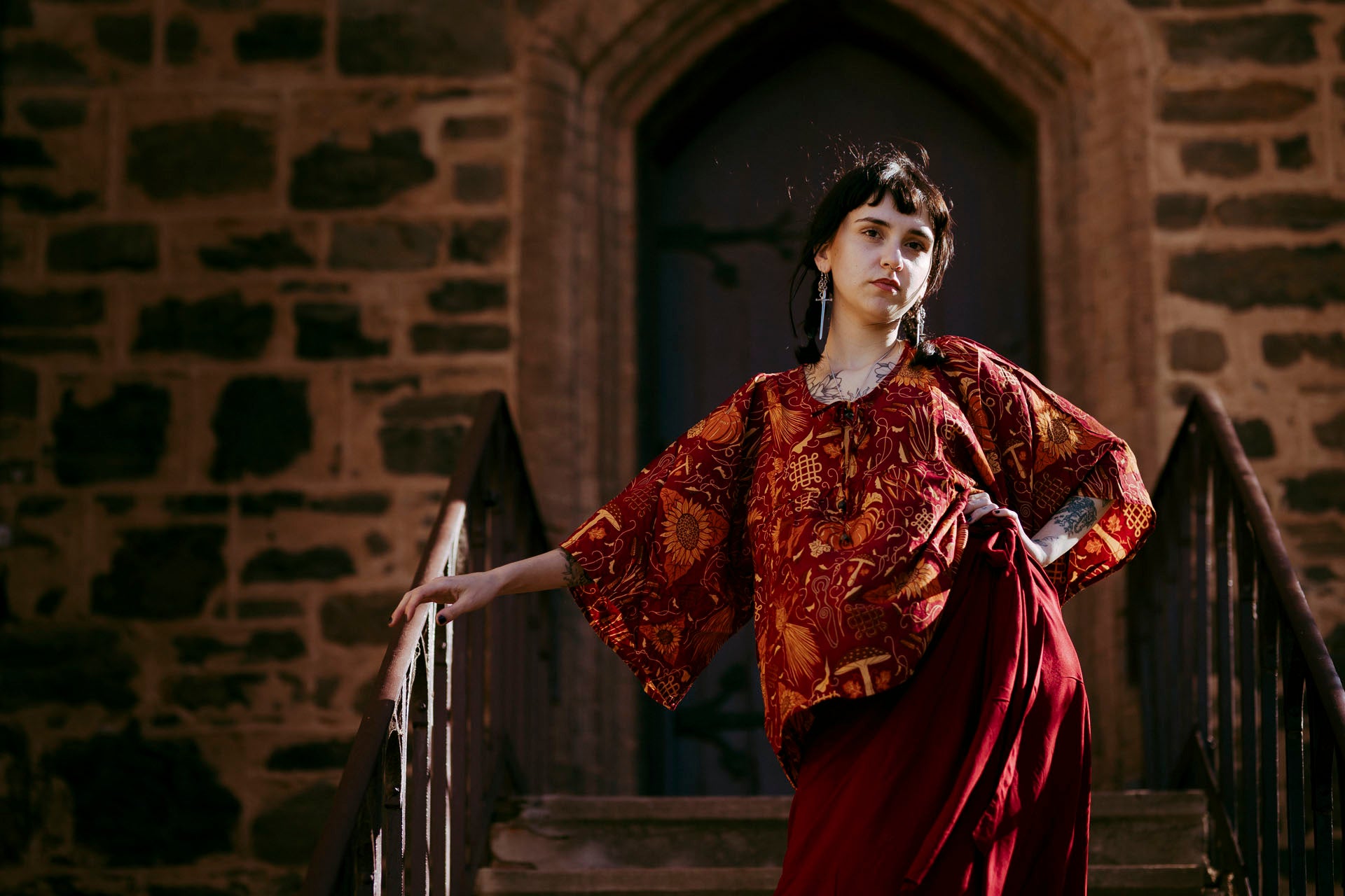 Woman in a red traditional outfit standing on stone steps with a stone building in the background