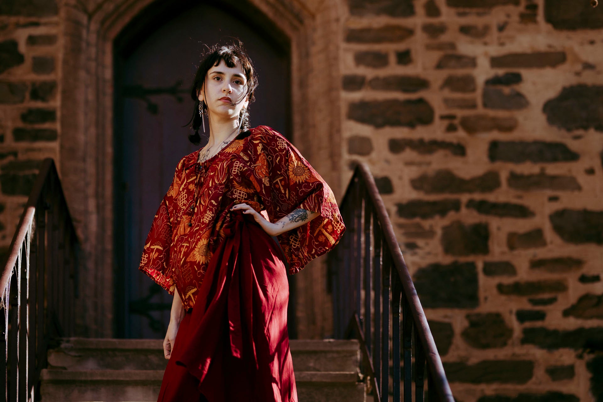 Woman in a red dress standing on stone steps with a stone wall background