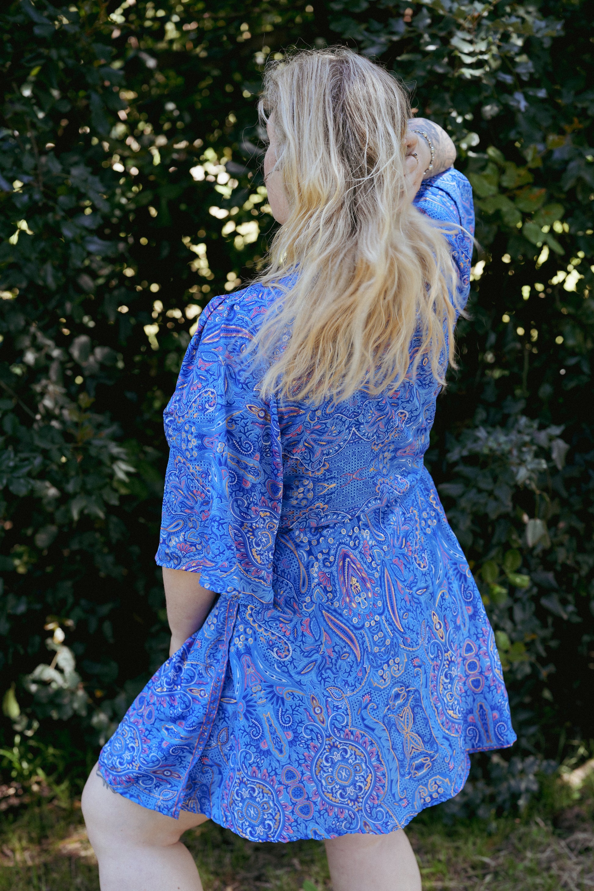 Woman wearing a blue patterned dress standing in front of green foliage