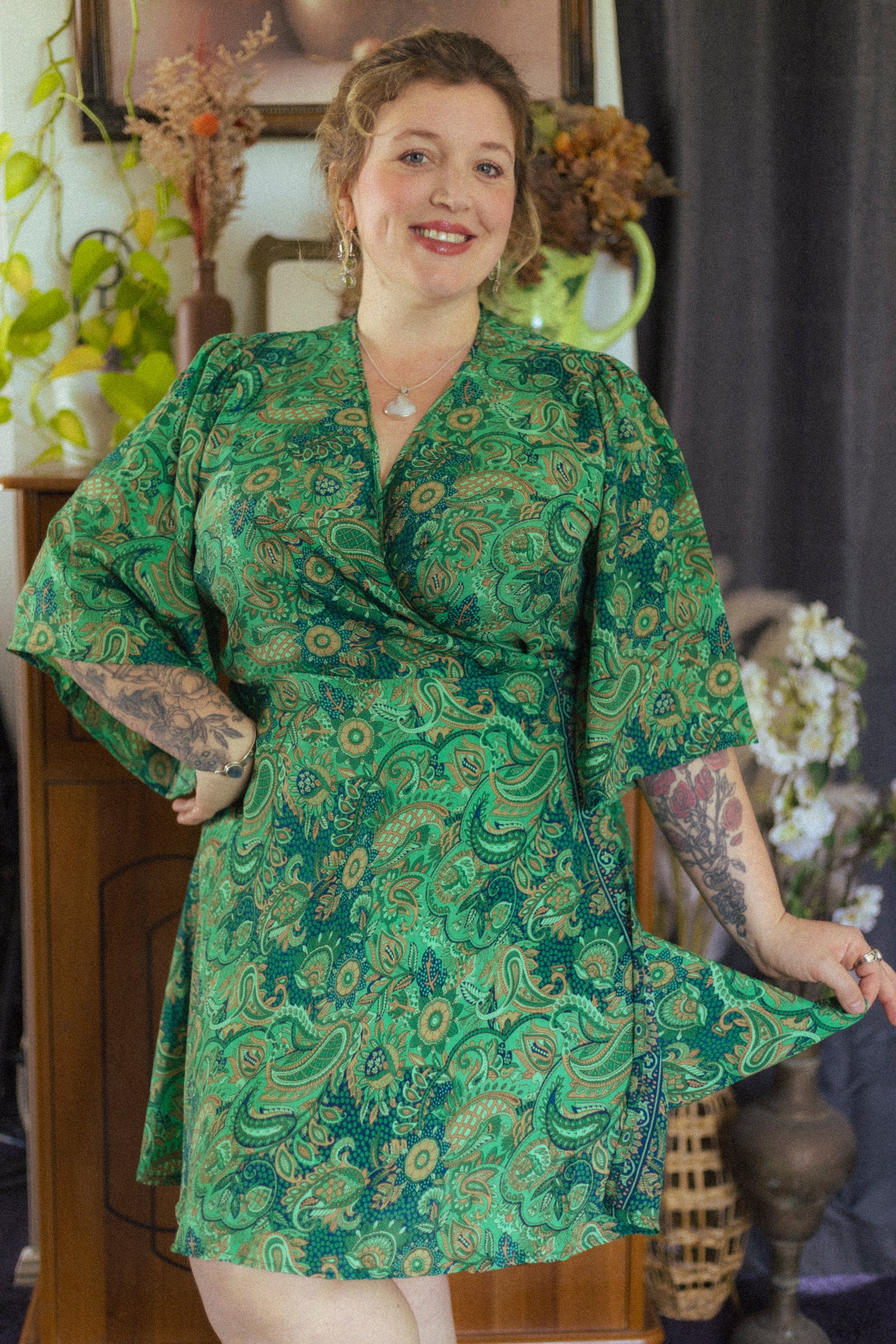 Woman wearing a green patterned dress in an indoor setting with plants and furniture.