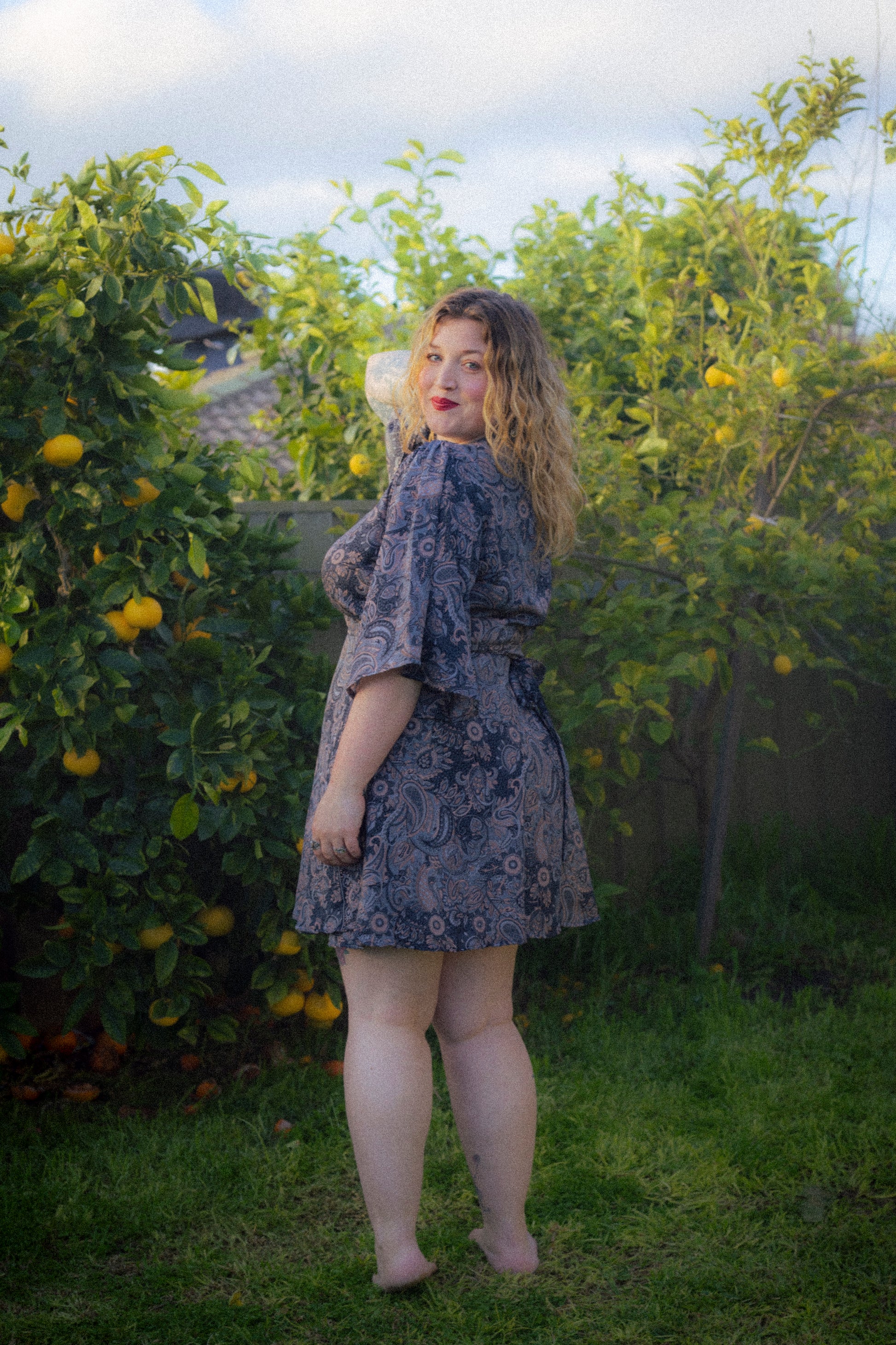 Woman in a floral dress standing in an orchard with lemon trees.