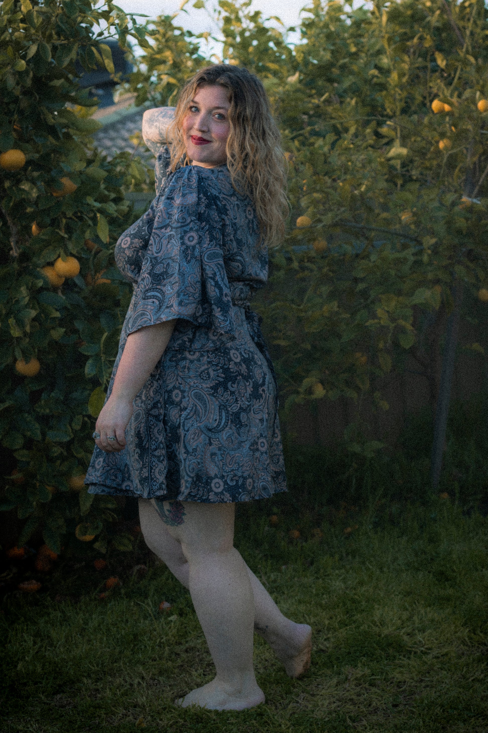 Woman in a patterned dress standing in a garden with fruit trees.