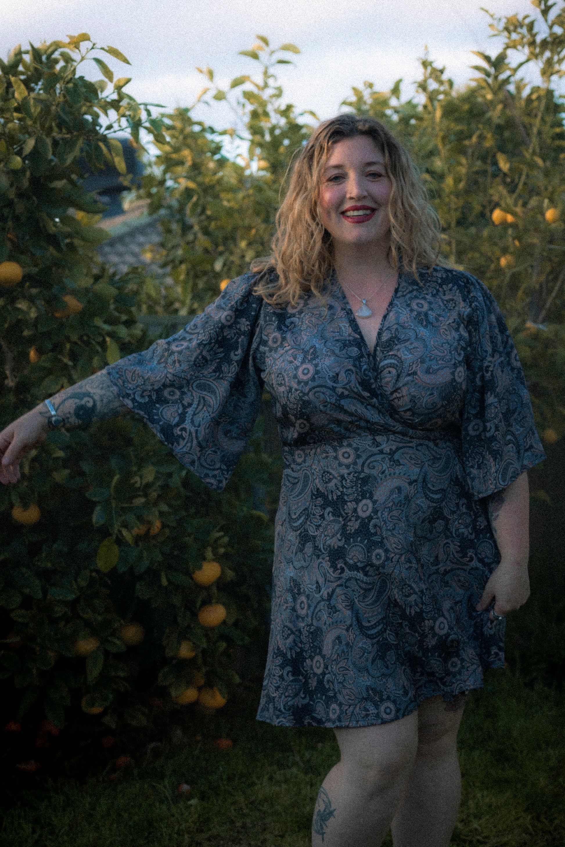Woman in a floral dress standing in an orchard with trees and fruit in the background