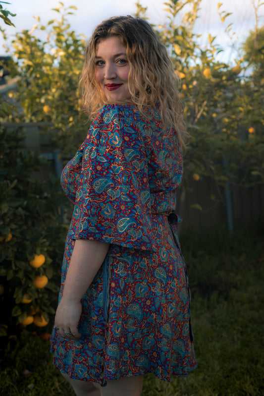 Woman wearing a colorful floral dress standing in a garden.