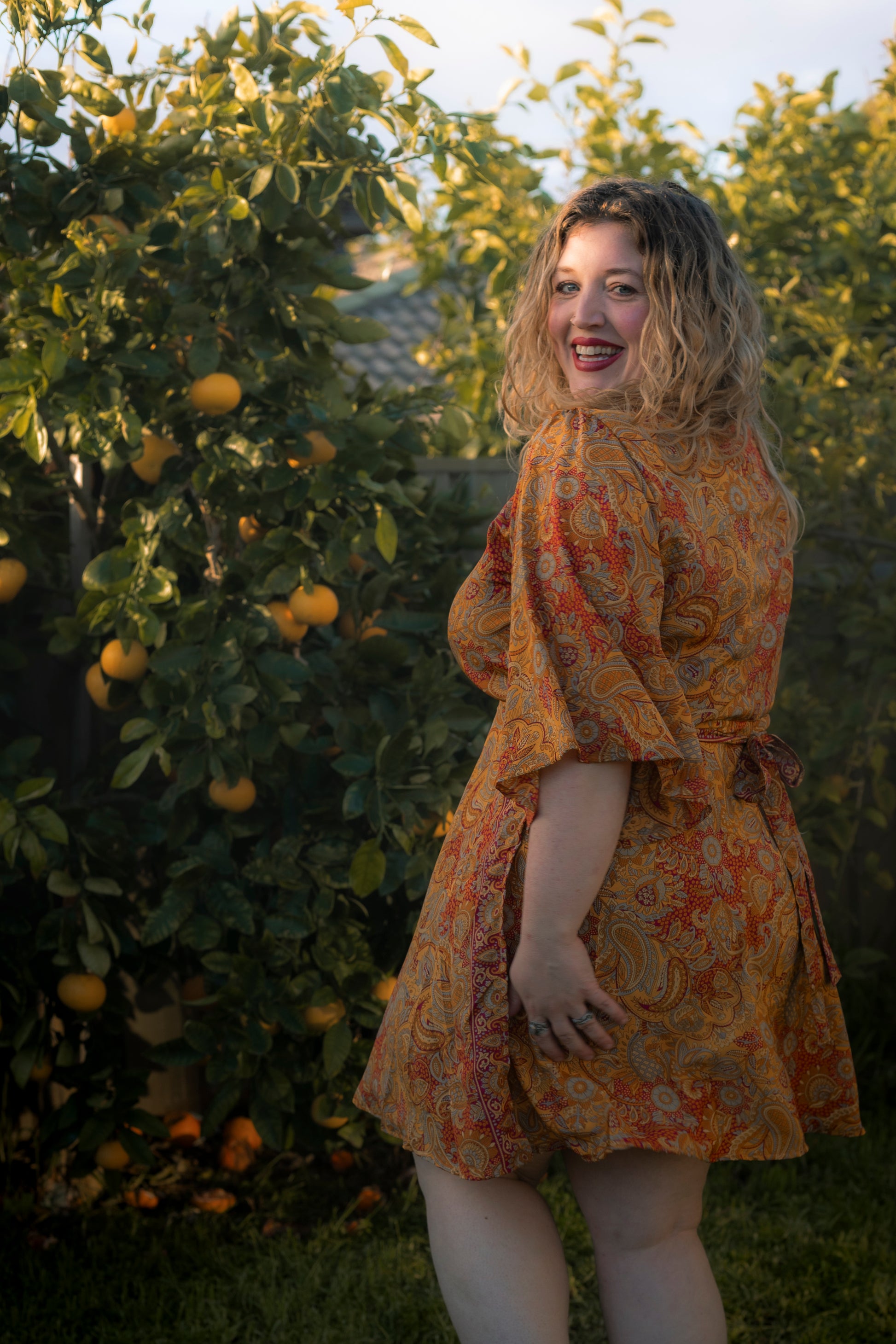 Woman in a patterned dress standing in an orchard with orange trees.