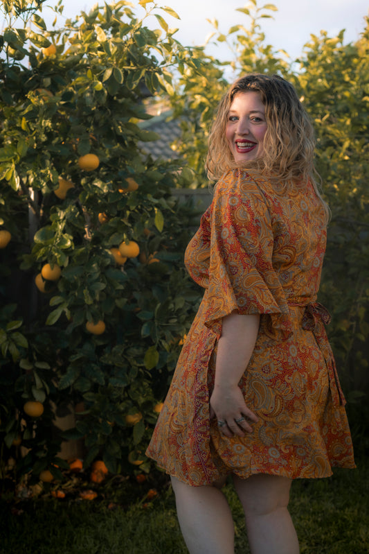 Woman in a patterned dress standing in an orchard with orange trees.
