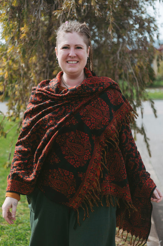 Woman wearing a patterned red shawl outdoors with trees and grass in the background
